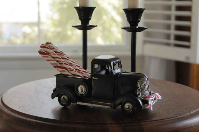 a toy truck that has candy canes sticking out of the truck bed perched on a table with two candlesticks in the background