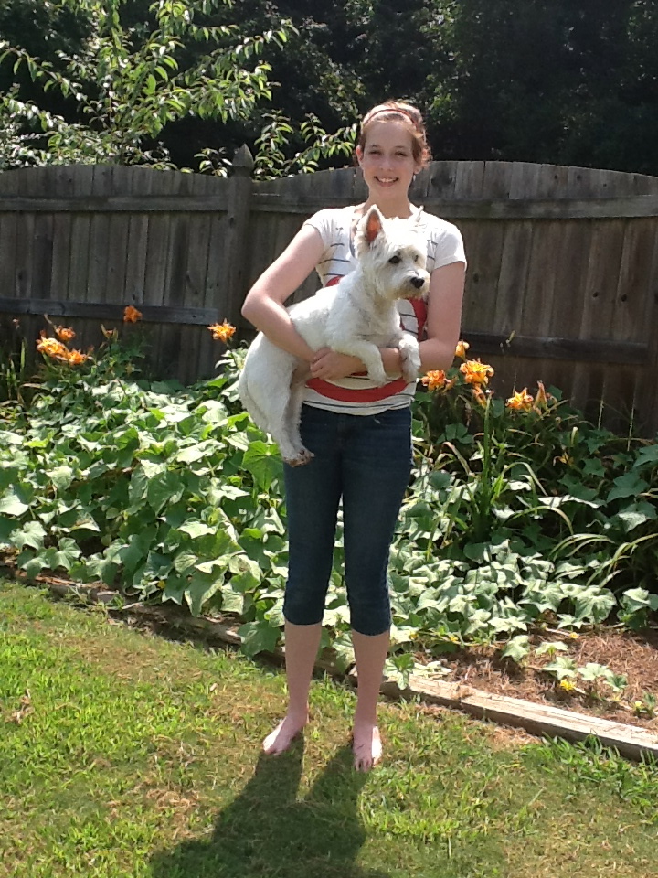 Girl standing in front of garden, holding white dog