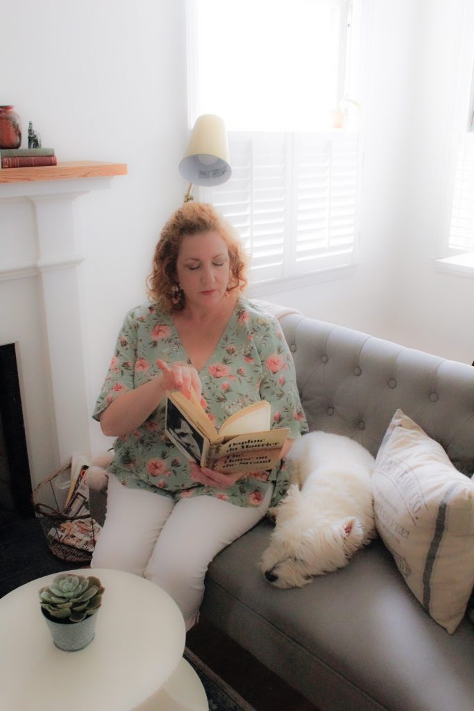 woman at home reading book by fireplace with dog sitting next to her