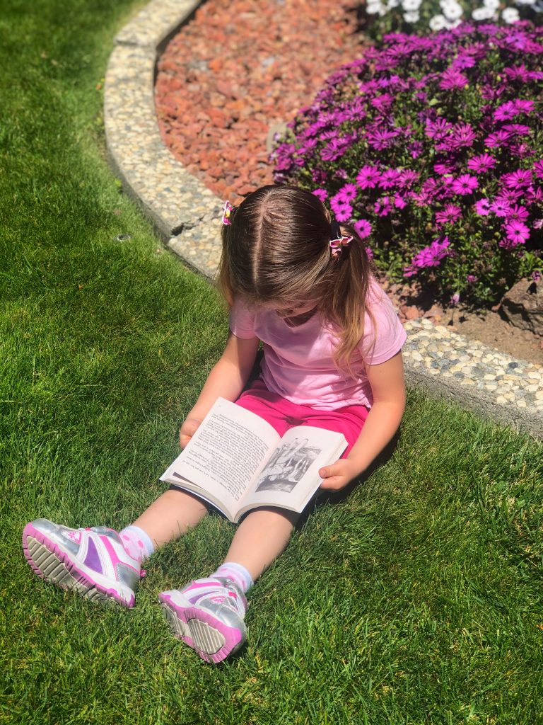 little girl sitting in the grass reading a book