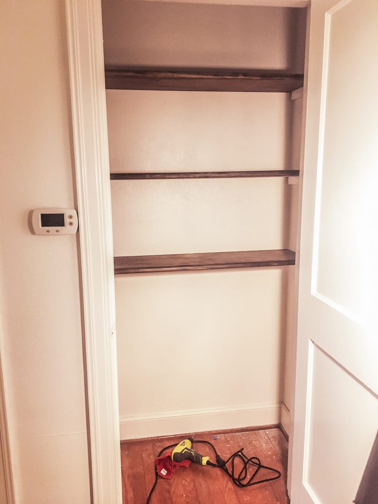 Newly-installed stained-wood shelves in a white-painted closet