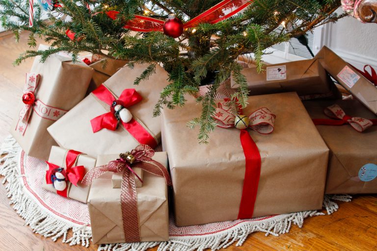 Presents wrapped in brown paper with red ribbons sit under a Christmas tree.